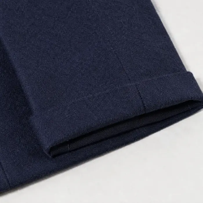 Extreme close-up of the turned-up hem of a navy wool trouser lying flat.