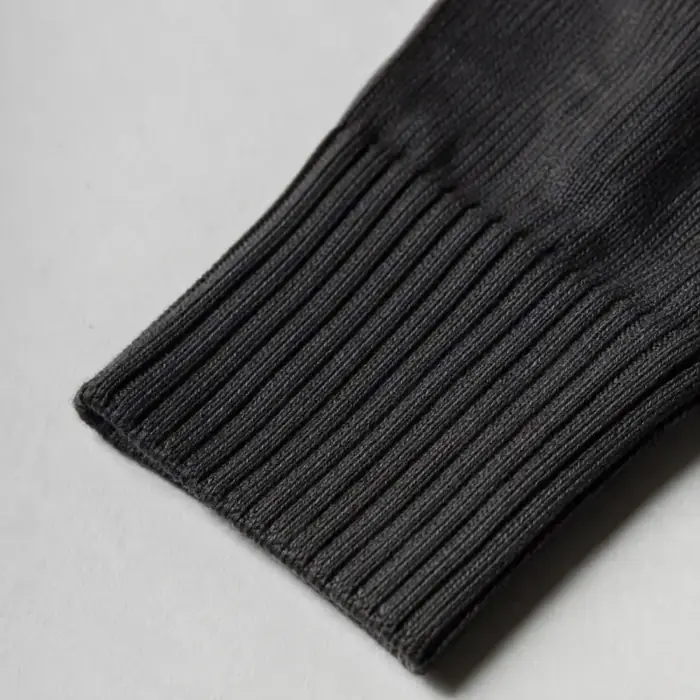 Extreme close-up of the ribbed cuff of a folded charcoal sock, the rib channels running across the frame.