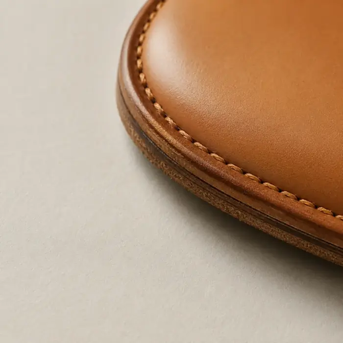 Extreme close-up of the welted edge of a tan leather shoe sole seen from the side on chalk paper.