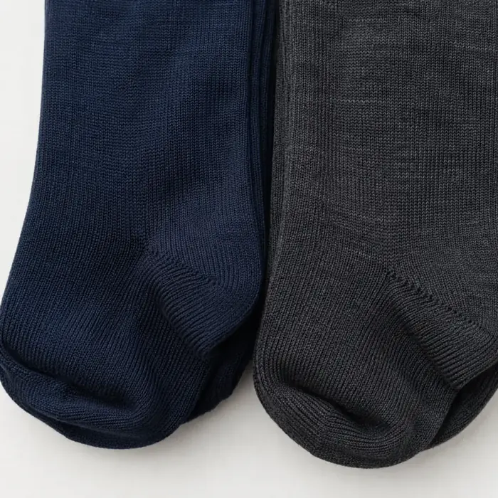 Extreme close-up of two folded socks laid edge to edge, one navy and one charcoal, the seam between them running down the middle of the frame.