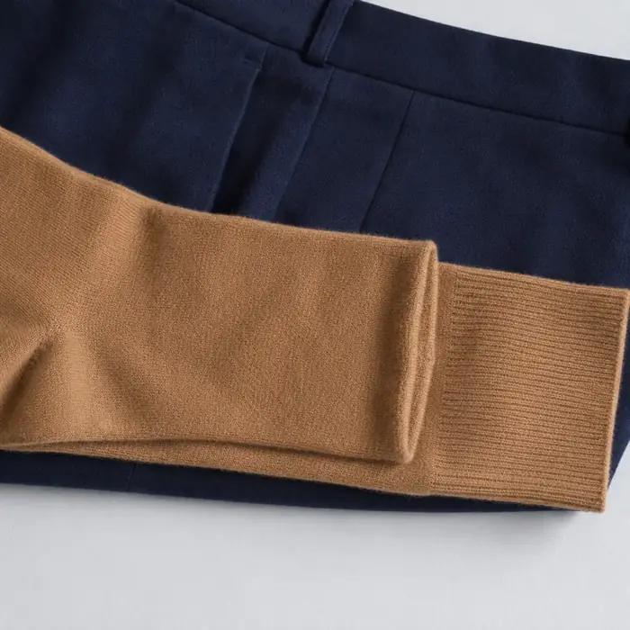 Extreme close-up of a folded camel cashmere sock lying across a folded navy wool trouser, the colour boundary crossing the frame horizontally.