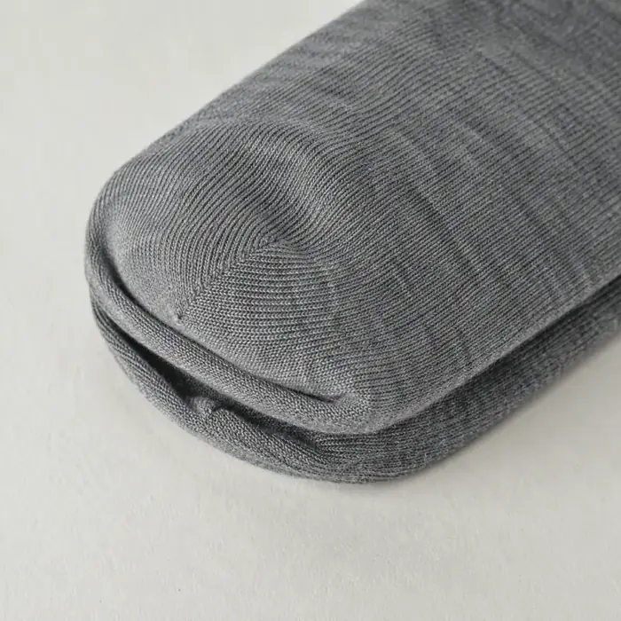 Extreme close-up of the heel of a rolled pair of grey merino socks on chalk paper.