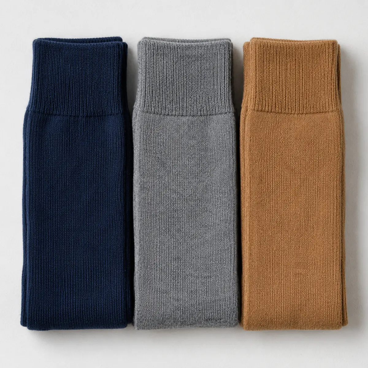Three folded pairs of socks in navy, mid grey and camel arranged as three parallel vertical bands touching edge to edge.