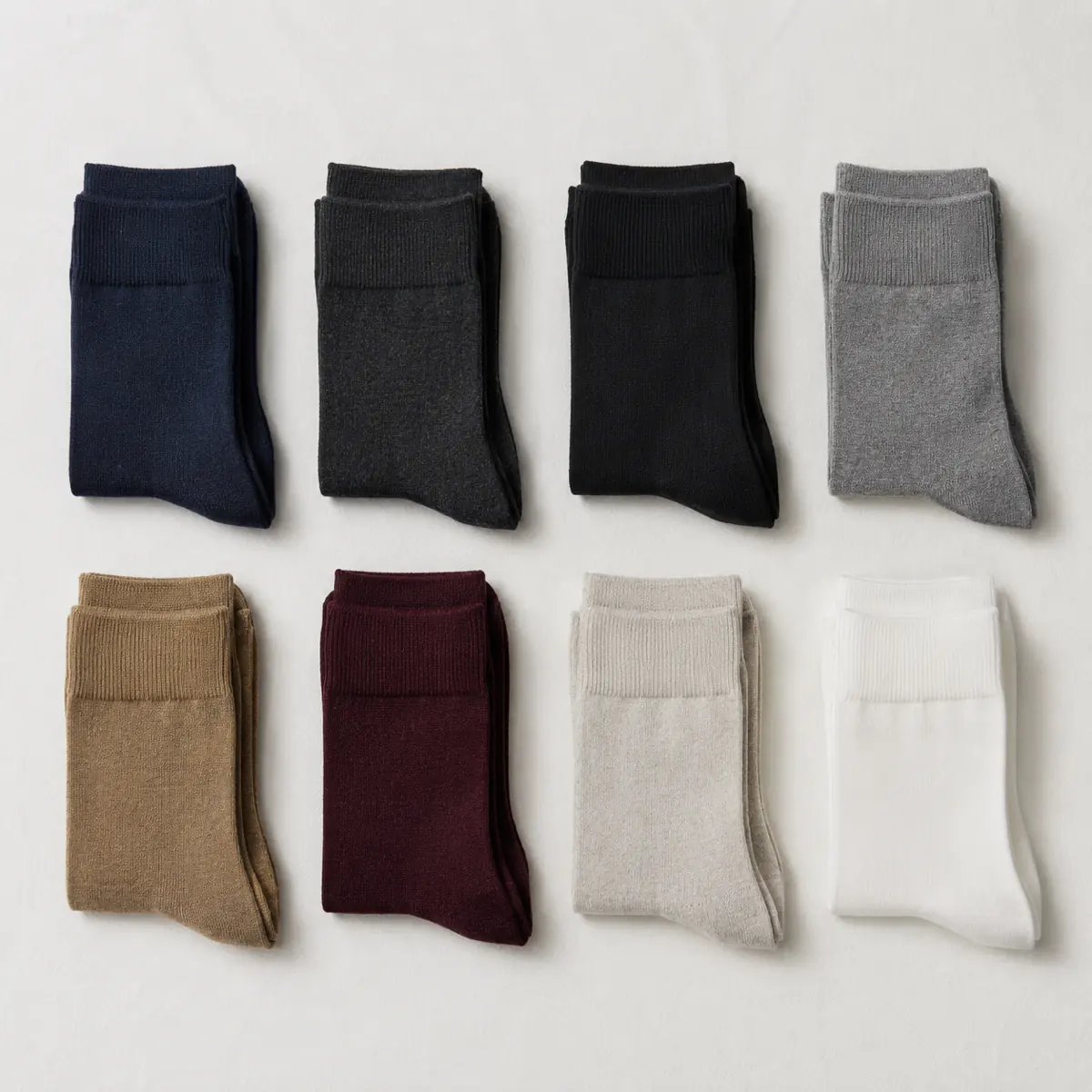 Eight pairs of folded socks in navy, charcoal, ink black, mid grey, camel, oxblood, pale stone and chalk white, arranged in a grid.