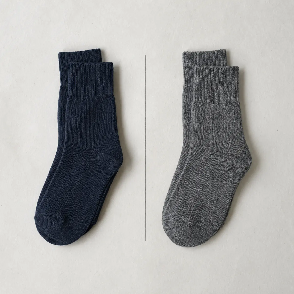 Two folded pairs of socks side by side, one navy and one mid grey, on a chalk paper sheet with a ruled line between them.