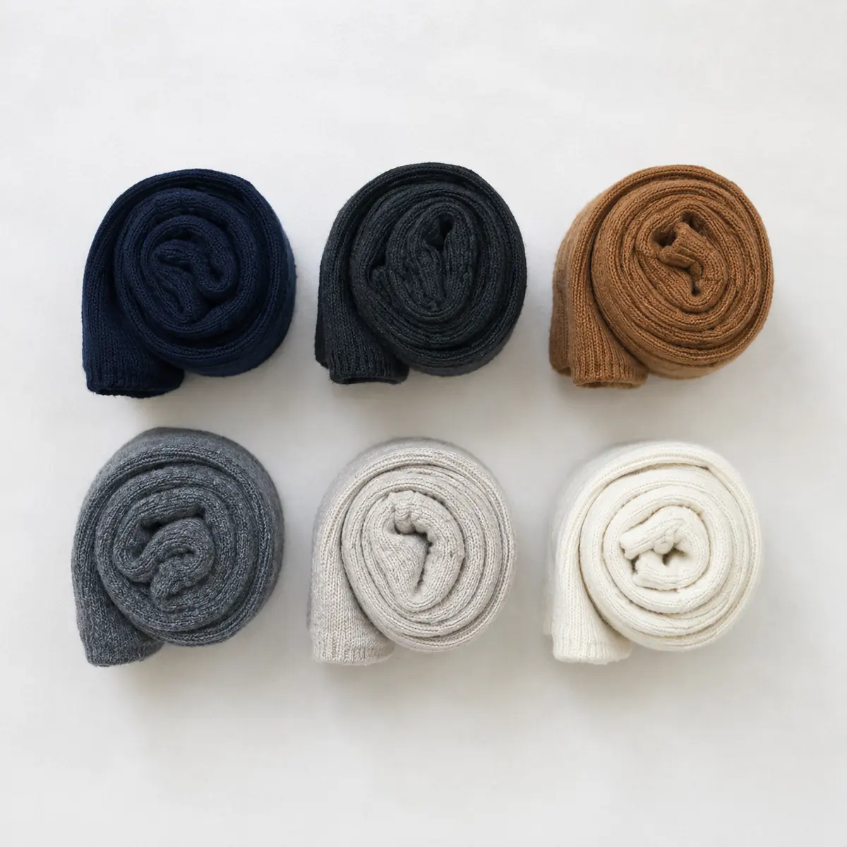 Six pairs of tightly rolled socks in two rows of three — navy, charcoal and camel above; grey, stone and chalk below.