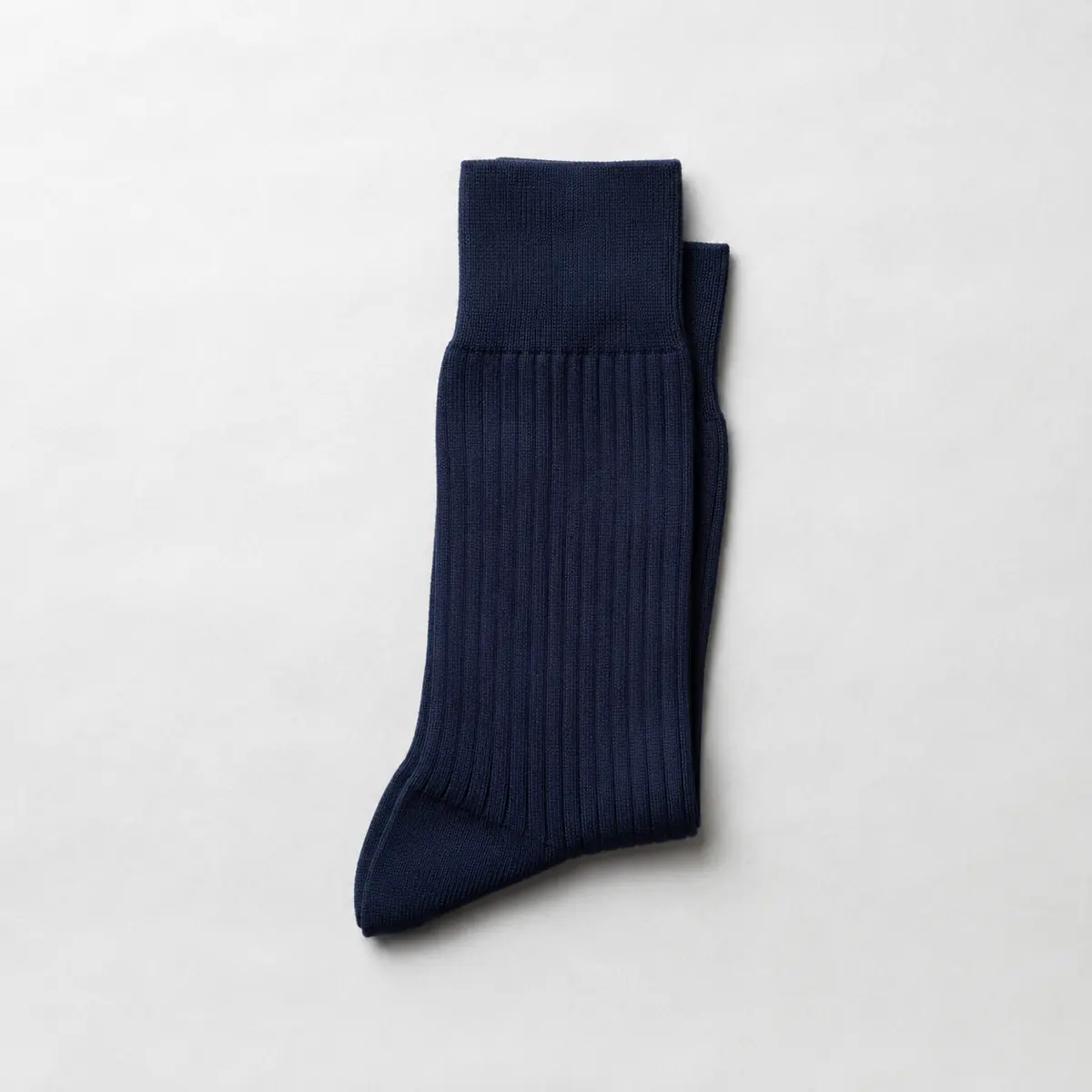 A single folded pair of deep navy over-the-calf socks lying alone in the centre of a large chalk paper sheet.