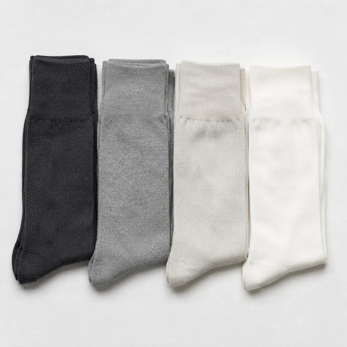 Four folded pairs of socks laid as four parallel vertical bands in charcoal, mid grey, pale stone and chalk white, stepping from dark to light.