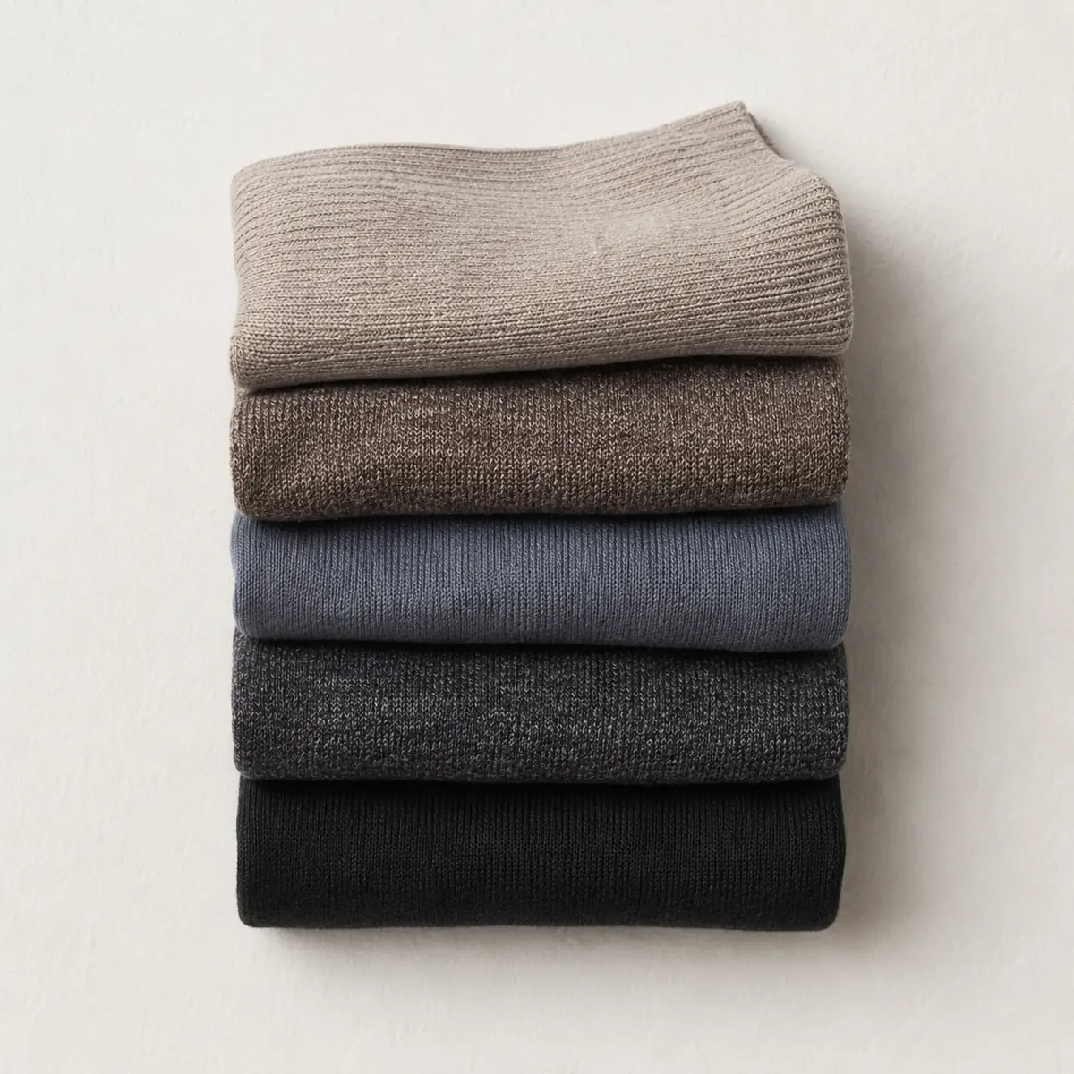 A neat stack of five folded pairs of socks seen from above, each a slightly different neutral, edges aligned.