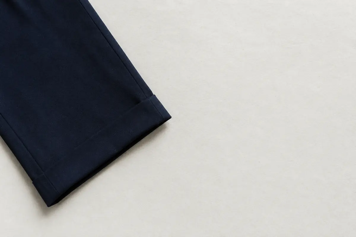 A folded navy trouser entering the frame from the left edge, the rest of the frame empty chalk paper.