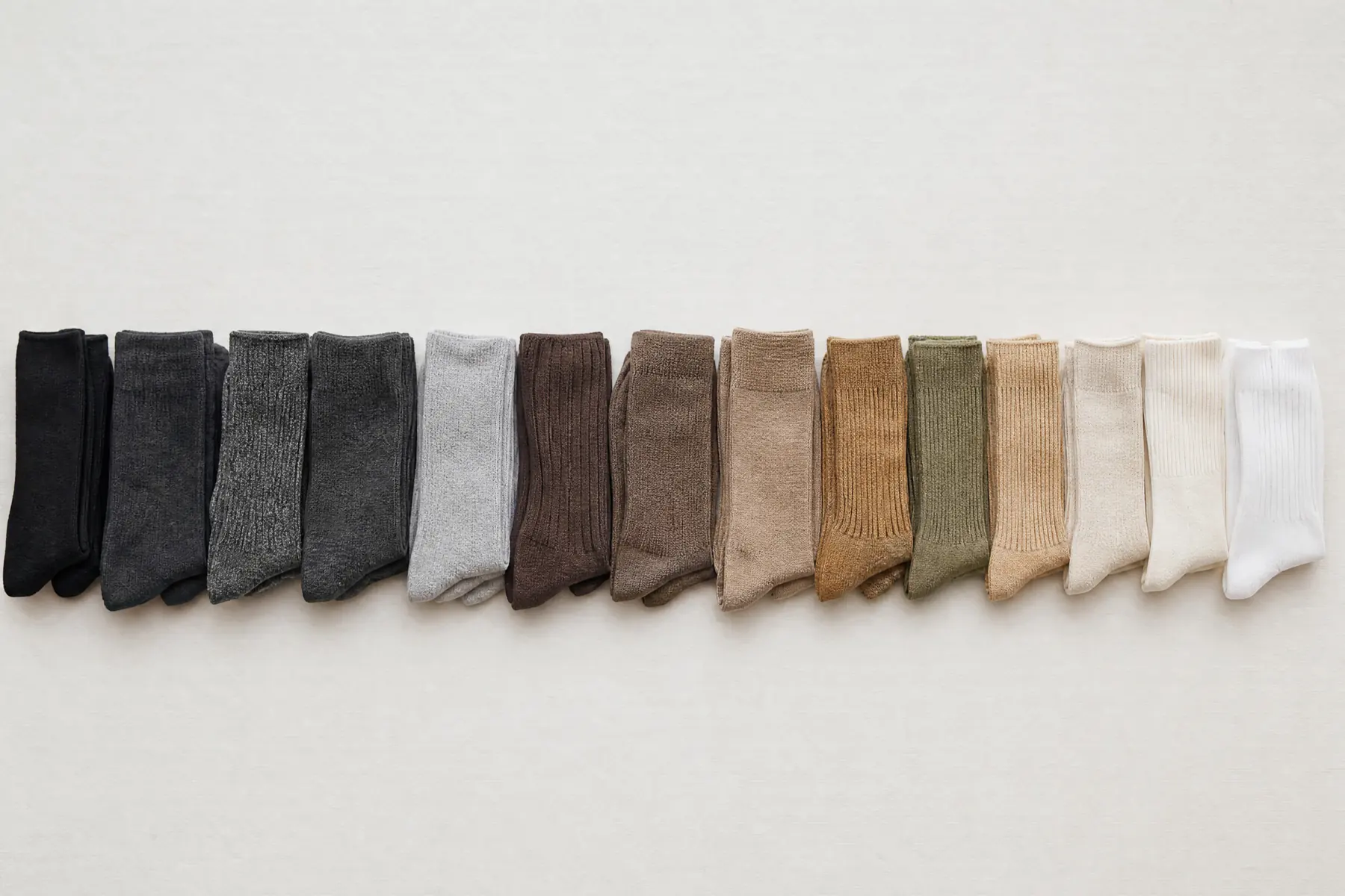 A wide overhead panorama of many folded socks arranged in a long single row running the full width of the frame, ordered dark to light.