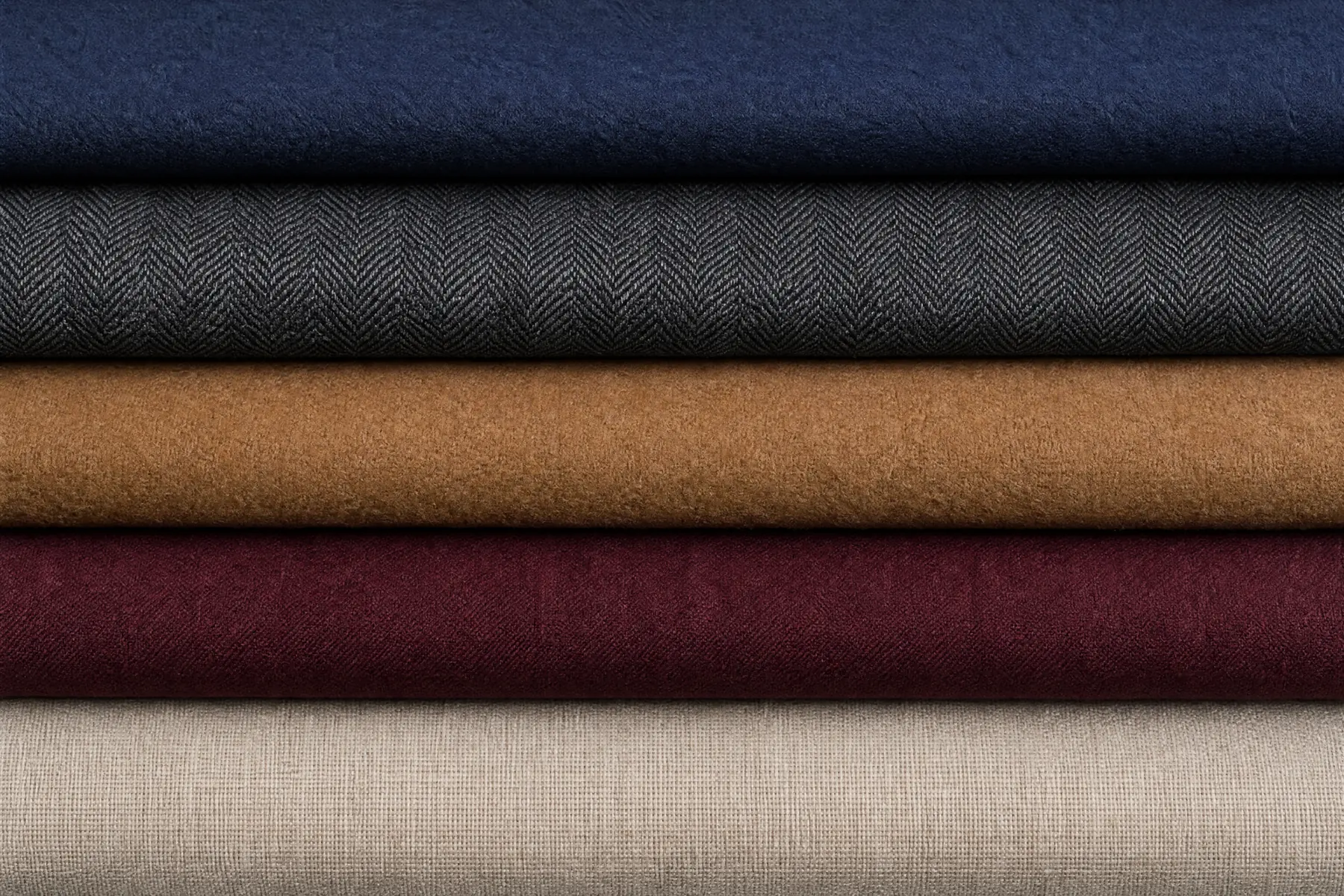 A wide overhead composition of folded menswear cloth in navy, charcoal, camel, oxblood and stone, laid as five long parallel horizontal bands filling the frame.